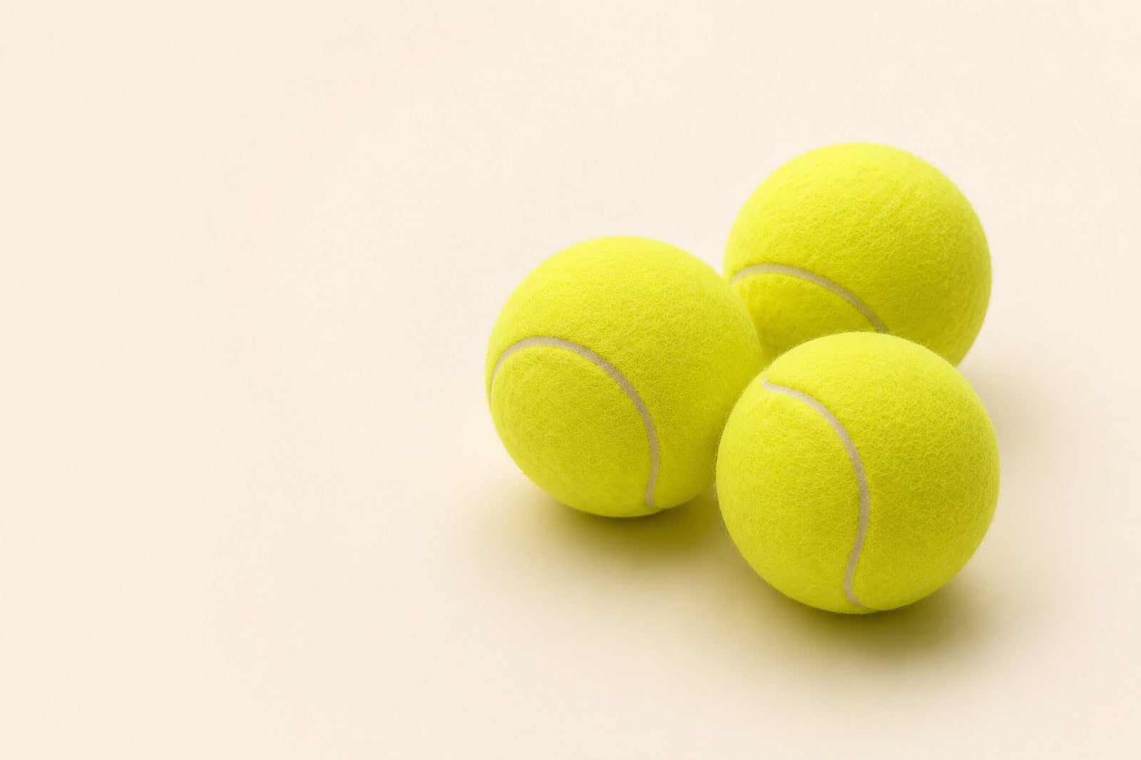 Three bright yellow tennis balls clustered together on a plain warm beige background.